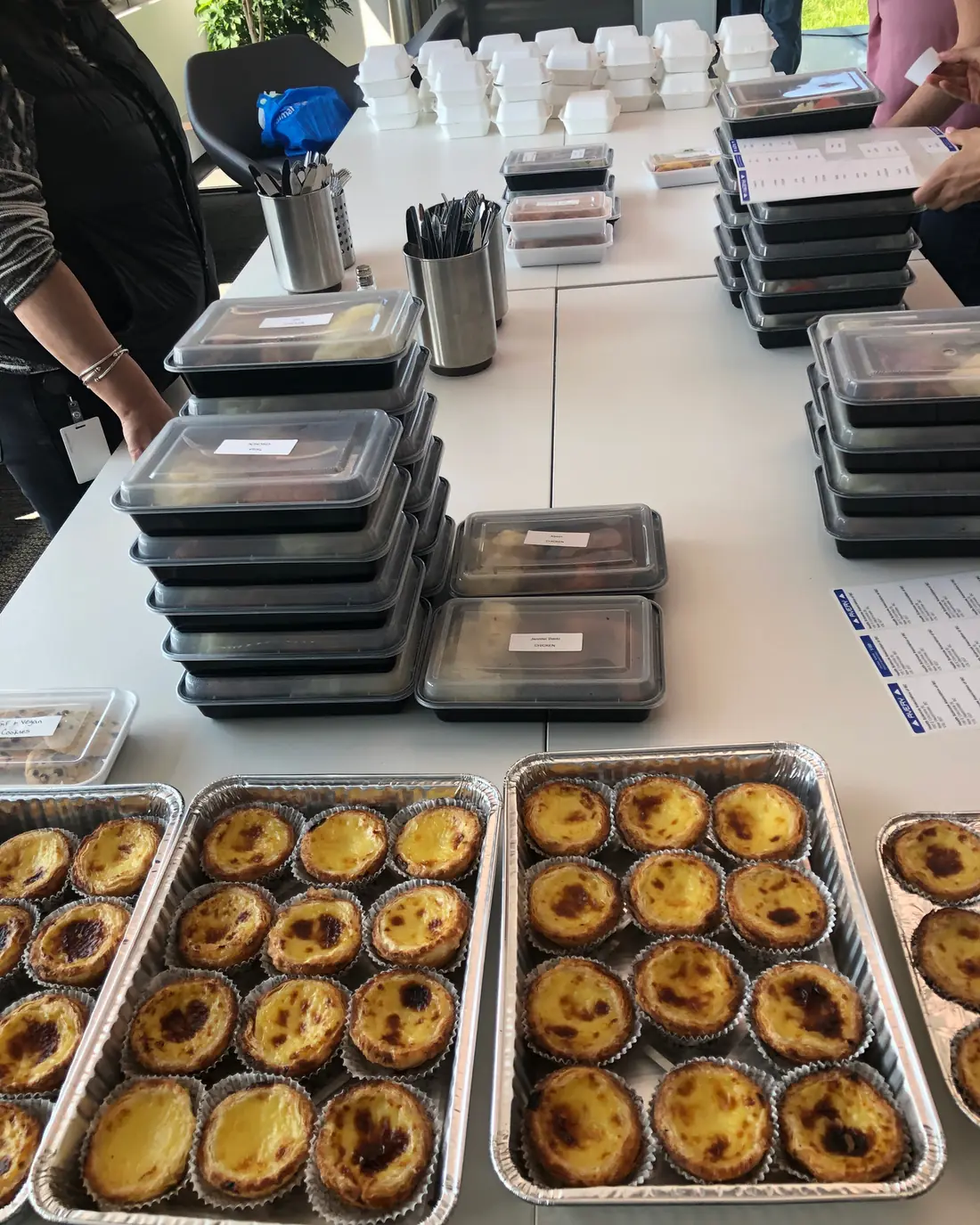 Trays of pastéis de nata beside stacks of sealed meal containers ready to go out.