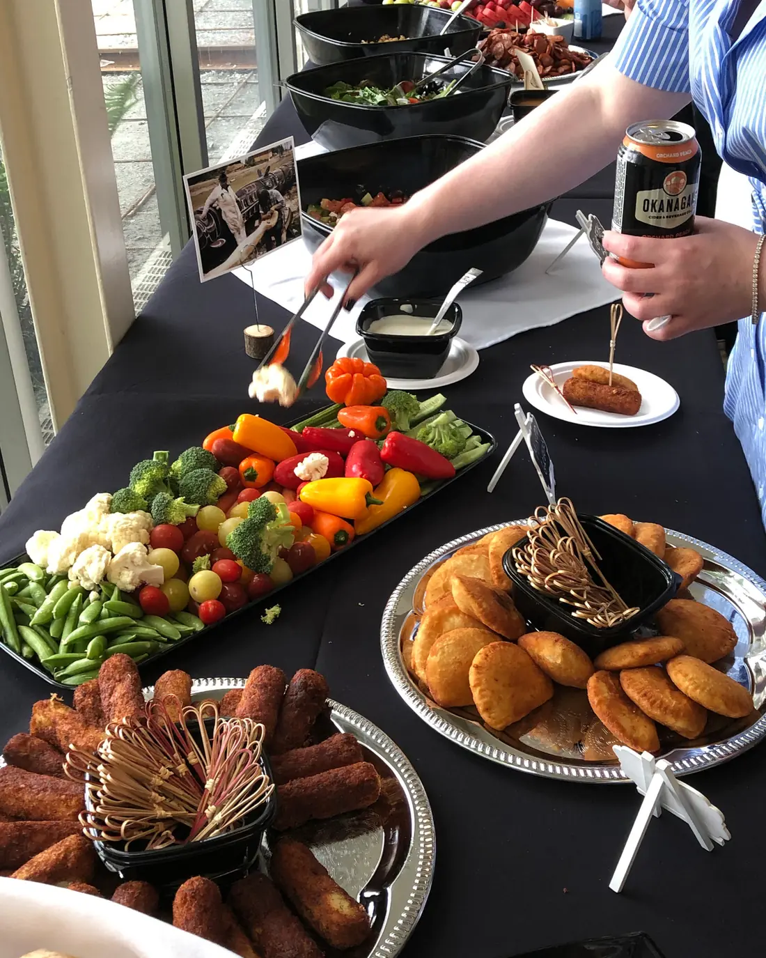 A long table of vegetable platters, chouriço and fried savouries, with guests helping themselves.
