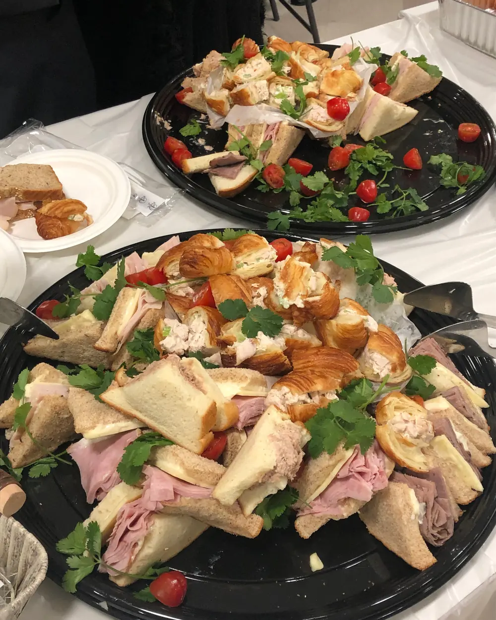 Round platters of assorted sandwiches and filled croissants garnished with tomato and herbs.